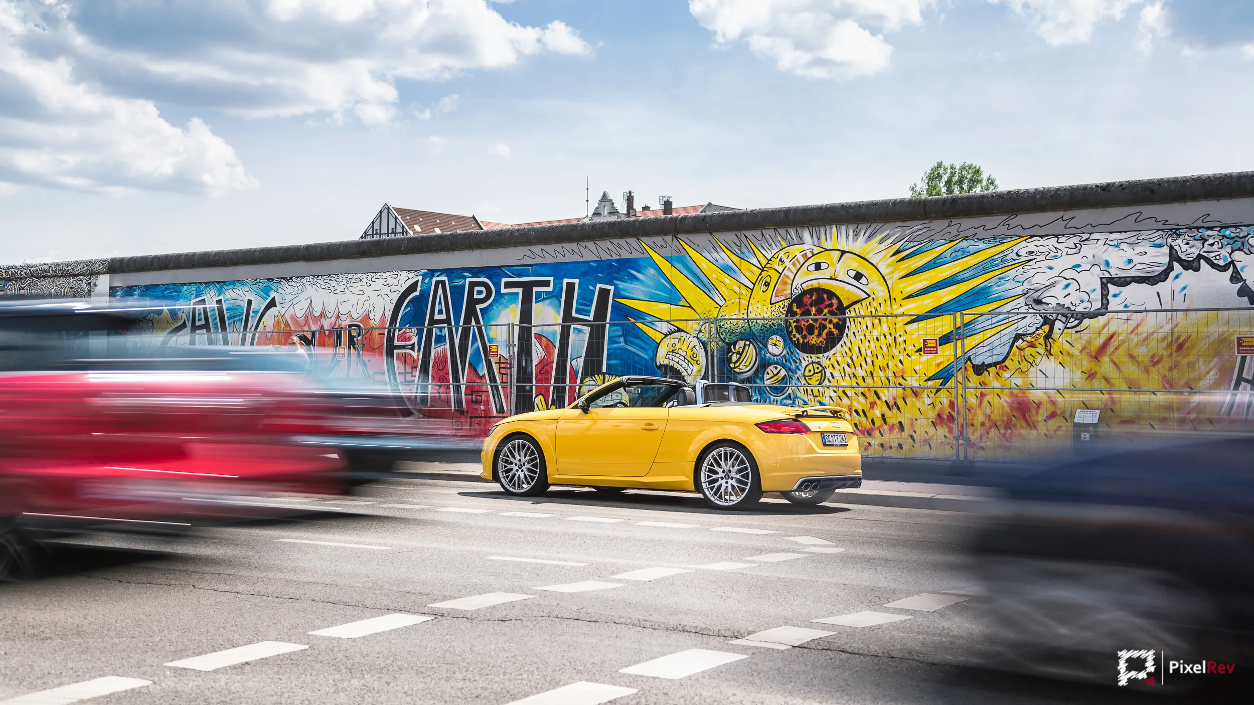 Gelber Audi TTS Roadster vor der East Side Gallery, vorbeifahrender Verkehr verwischt