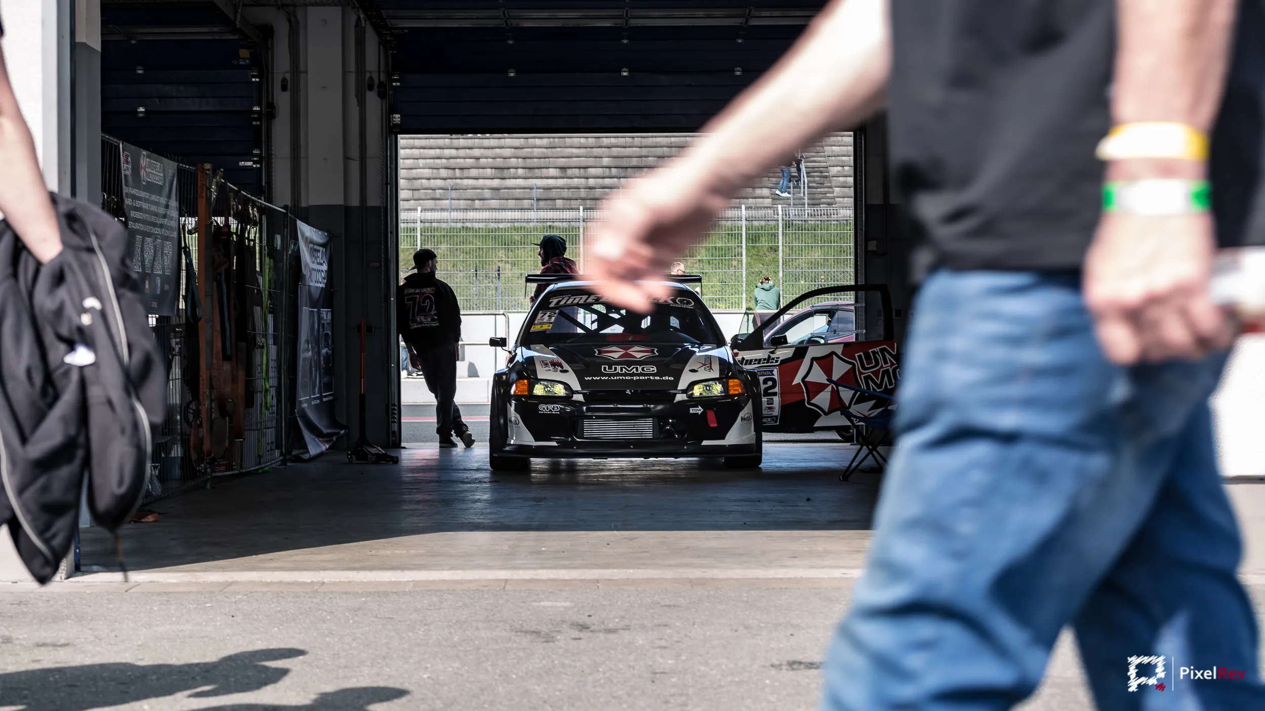 Blick in eine Box mit Rennwagen, im Vordergrund vorbeigehende Besucher