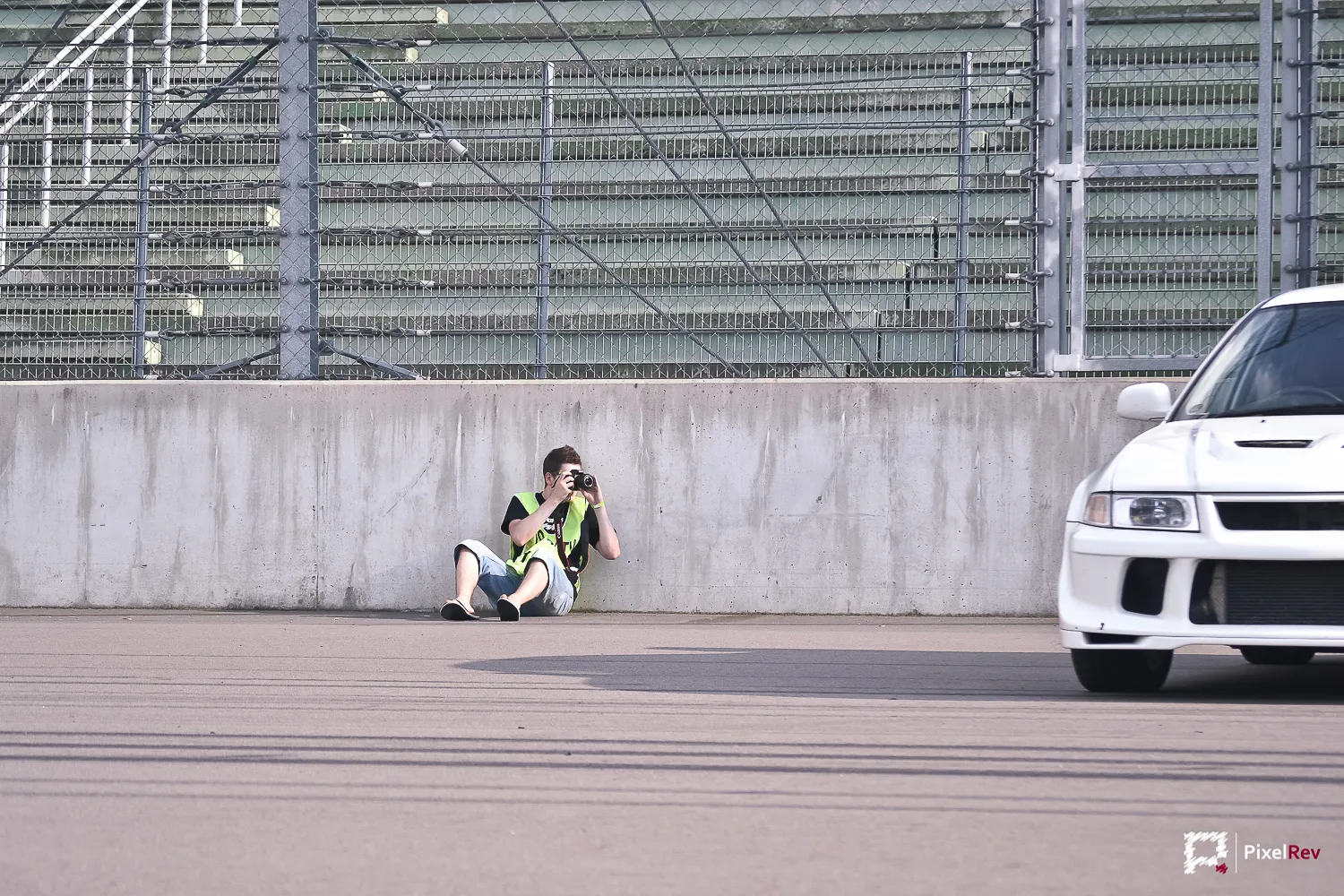 Fotograf sitzt vor der Boxenmauer, rechts ein weißer Mitsubishi Lancer Evolution VI