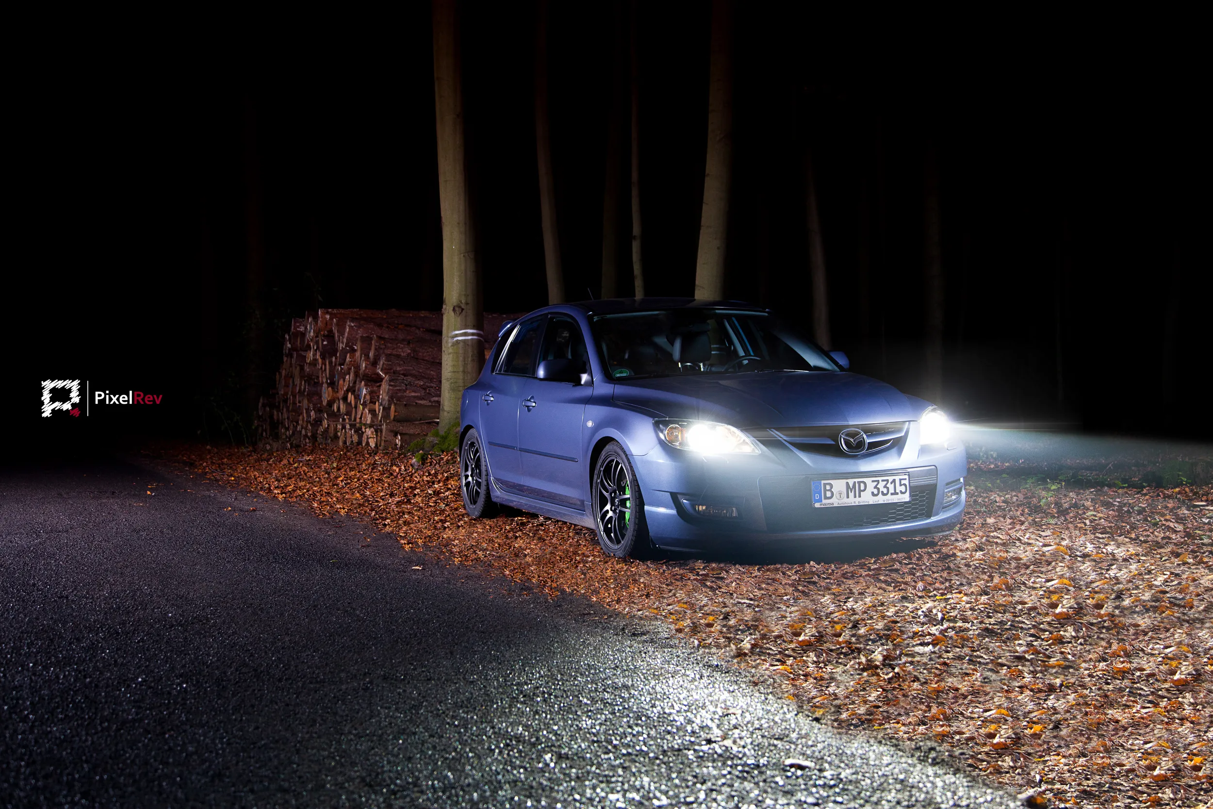 Mazda 3 MPS mit eingeschalteten Scheinwerfern nachts im Wald auf Herbstlaub