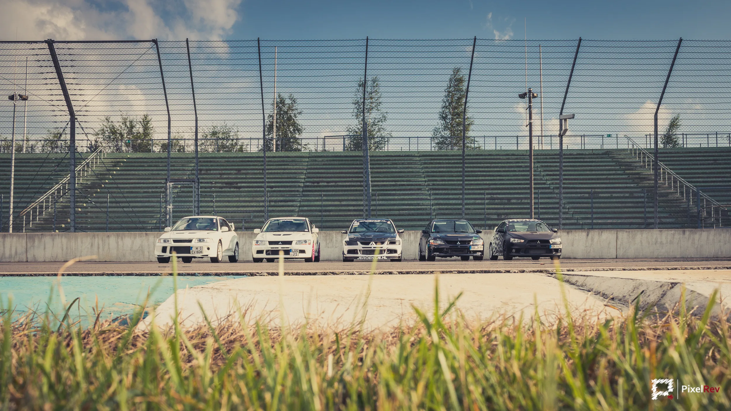 Mitsubishi Lancer Evolution in einer Reihe vor der Tribüne, Gras im Vordergrund