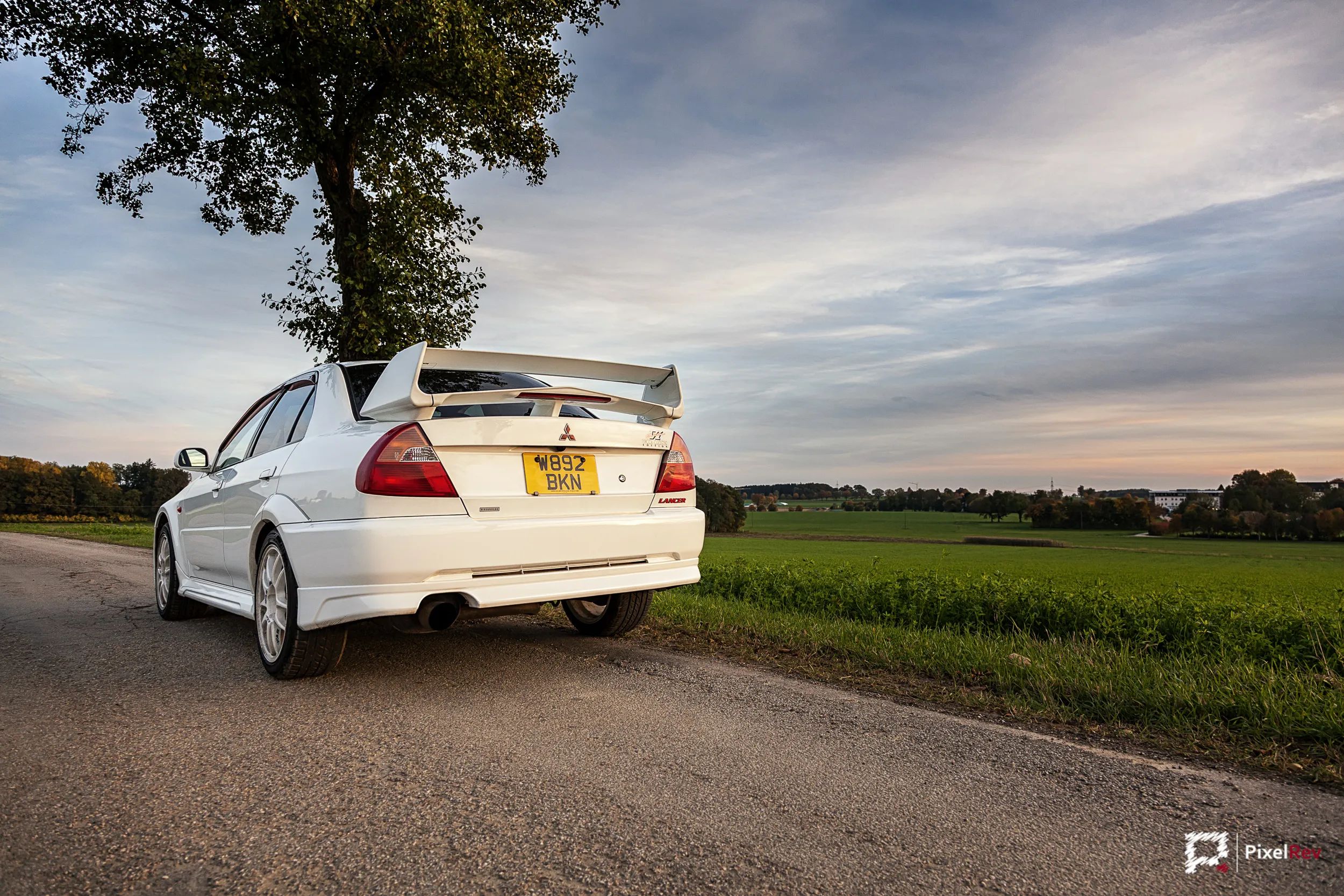 Heck eines weißen Mitsubishi Lancer Evolution VI mit großem Heckflügel unter einem Baum