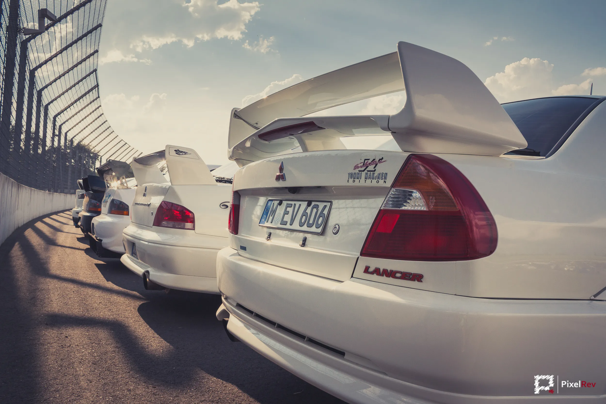 Heck eines weißen Mitsubishi Lancer Evolution VI, dahinter weitere Evos in einer Reihe