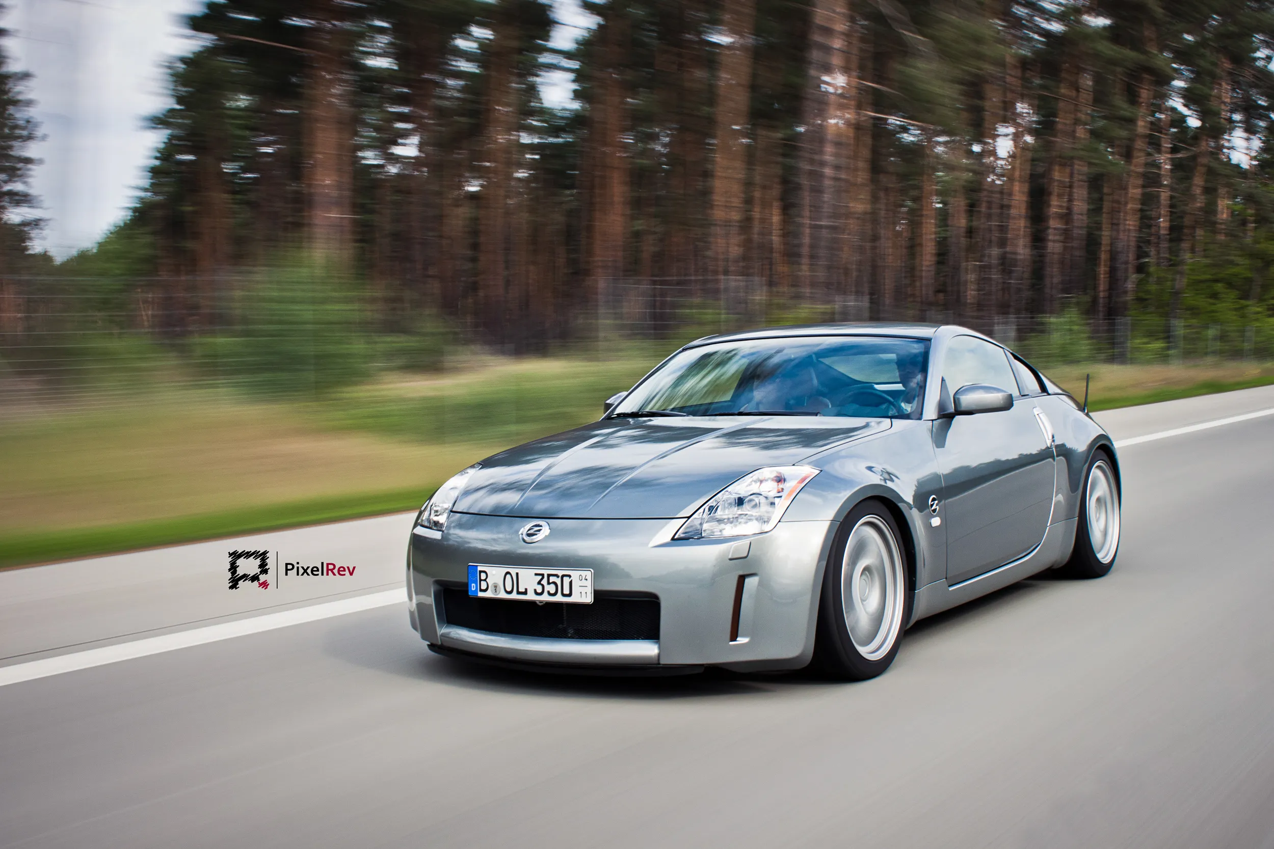 Silberner Nissan 350Z in Fahrt vor verwischtem Kiefernwald