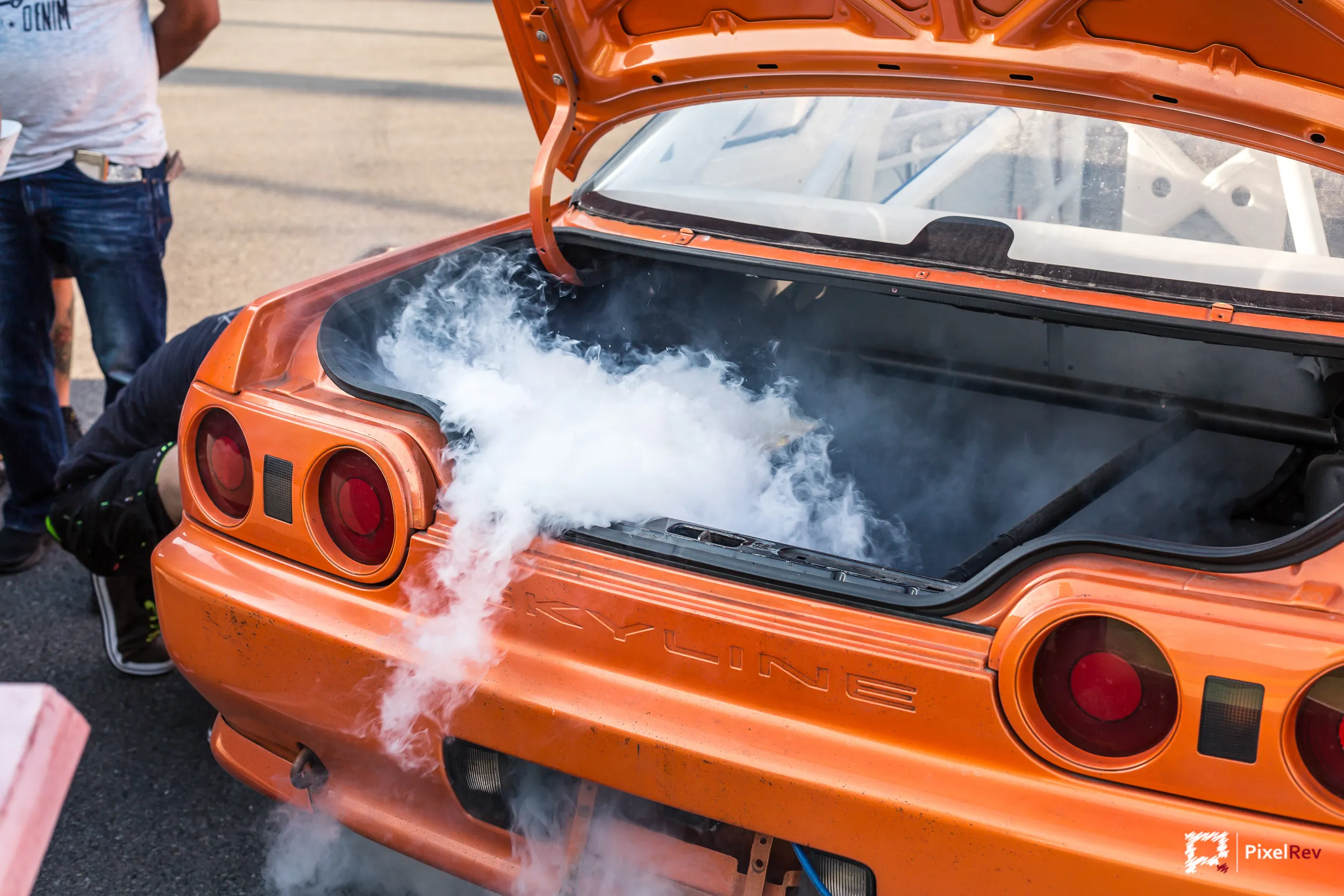 Orangefarbener Nissan Skyline R32 mit Rauch aus dem offenen Kofferraum