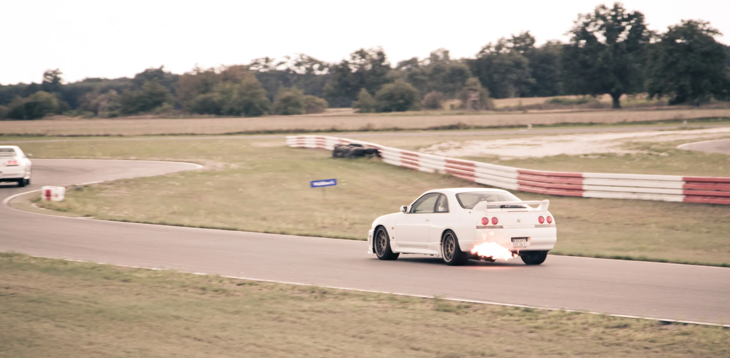 Weißer Nissan Skyline R33 mit Flammen aus dem Auspuff auf der Rennstrecke