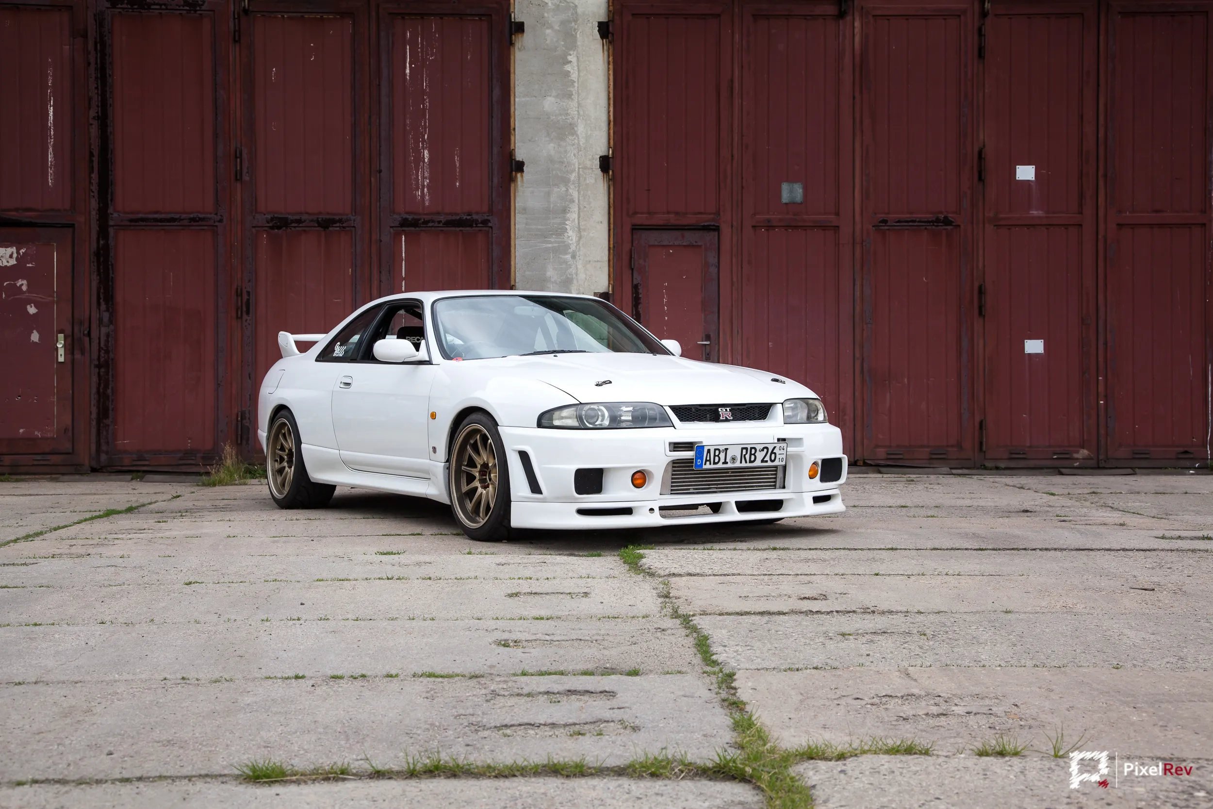 Weißer Nissan Skyline R33 GT-R frontal vor roten Hangartoren
