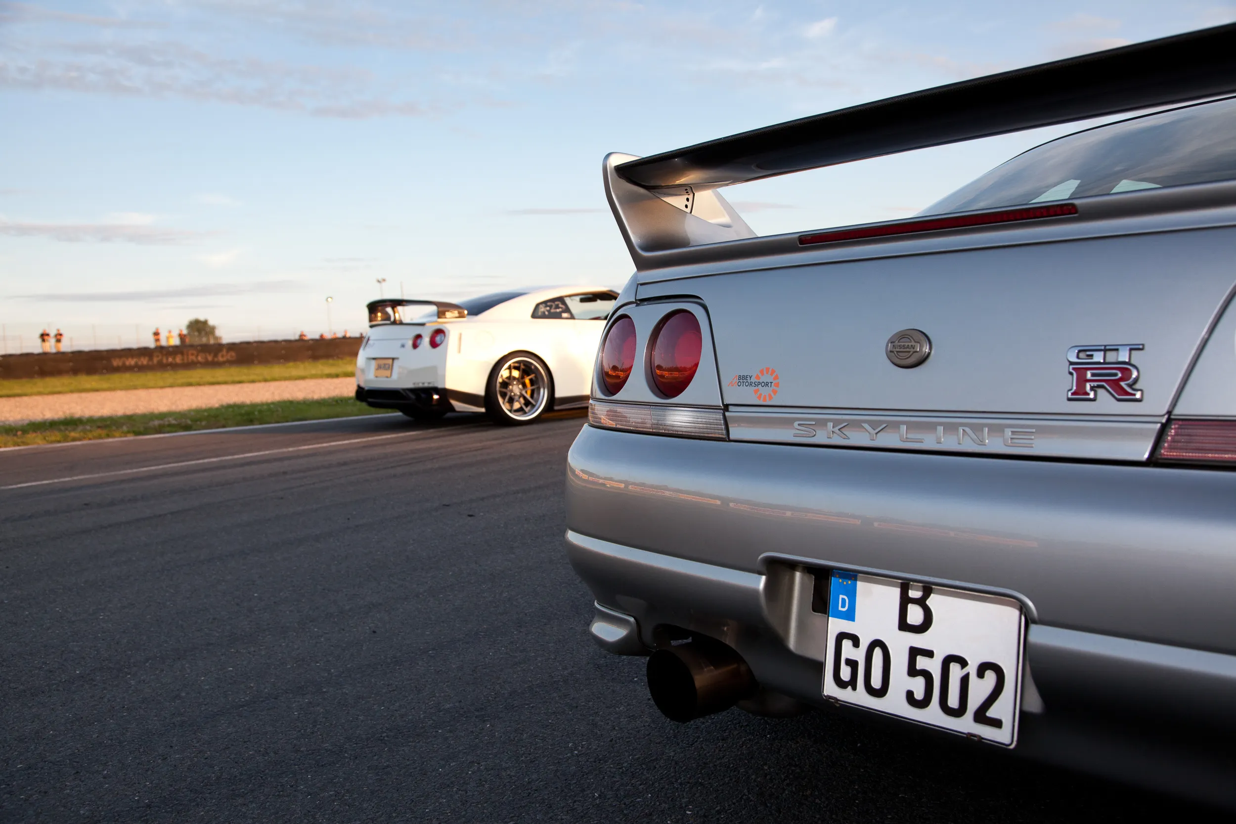 Heck eines silbernen Nissan Skyline R33 GT-R, dahinter ein weißer Nissan GT-R