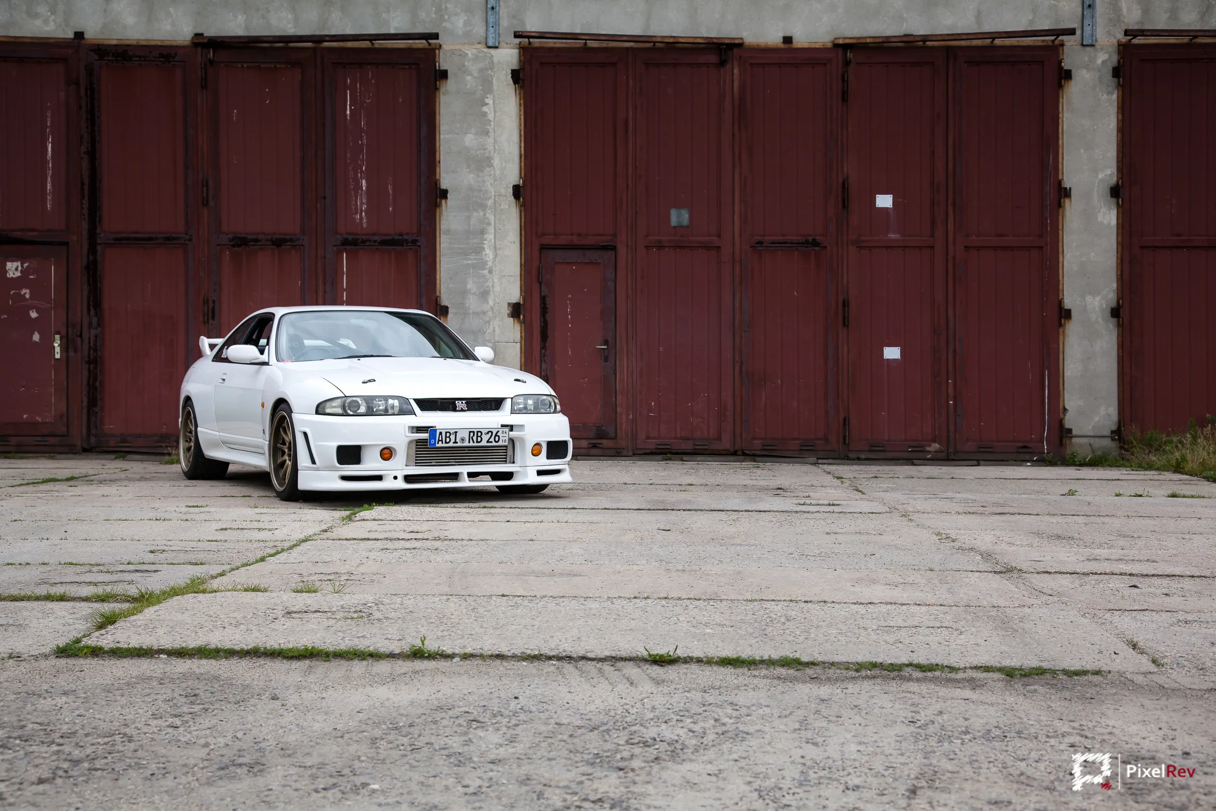 Weißer Nissan Skyline R33 GT-R mit goldenen Felgen vor roten Toren