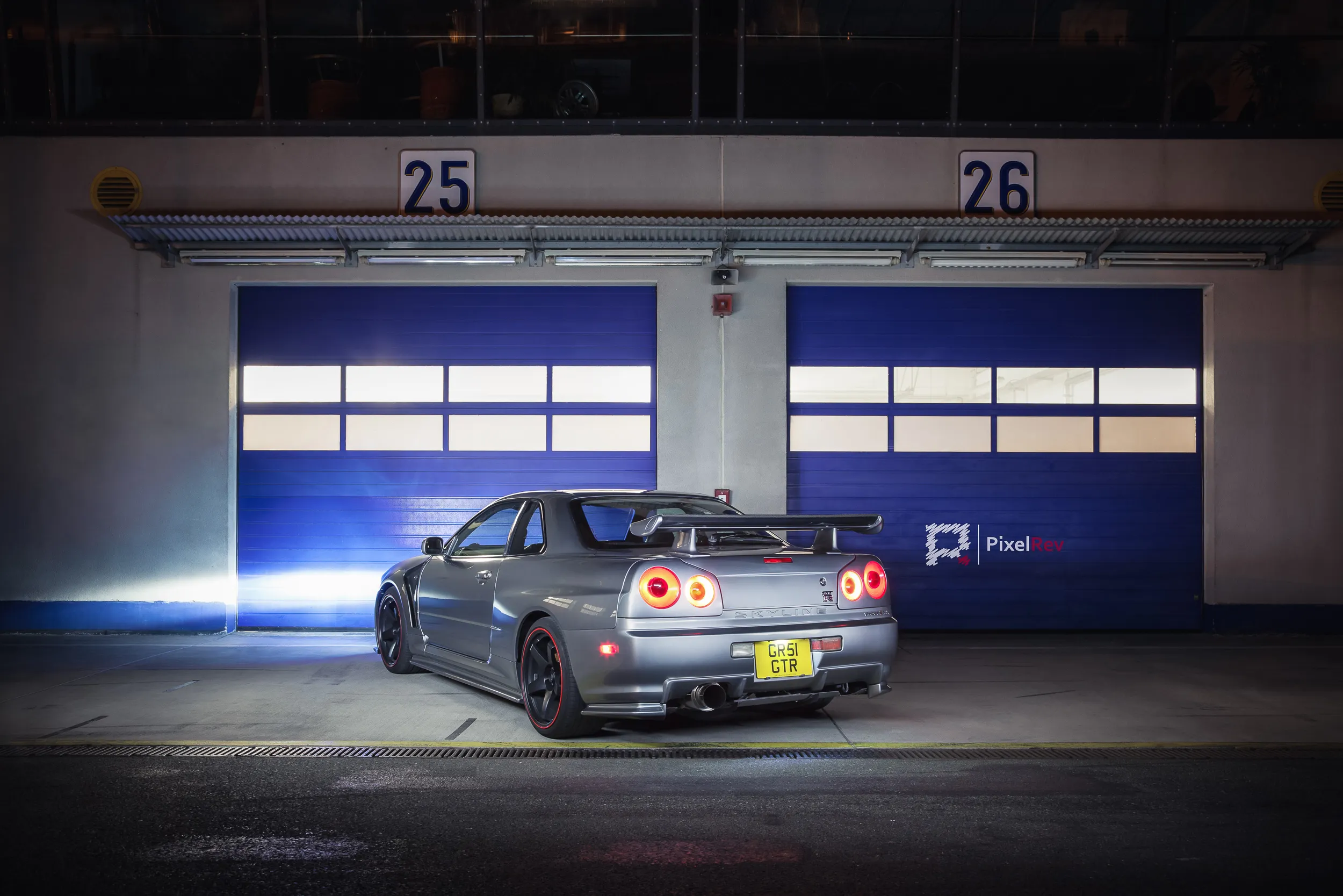Grauer Nissan Skyline R34 GT-R vor den Boxen bei Nacht