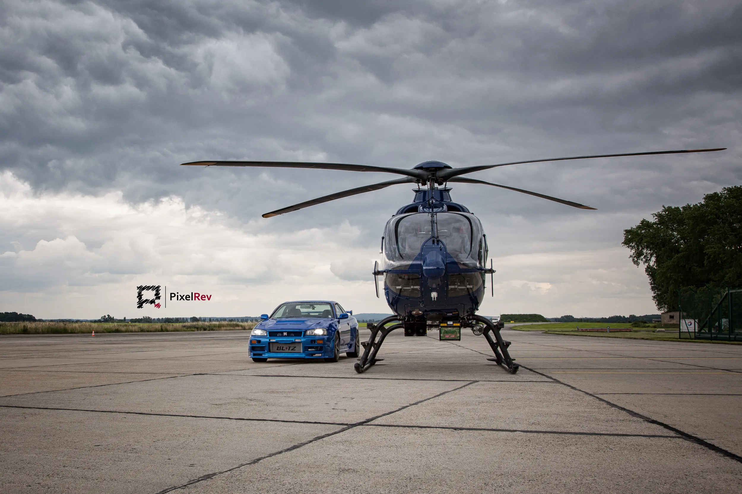 Hubschrauber frontal, daneben der blaue Nissan Skyline R34 GT-R