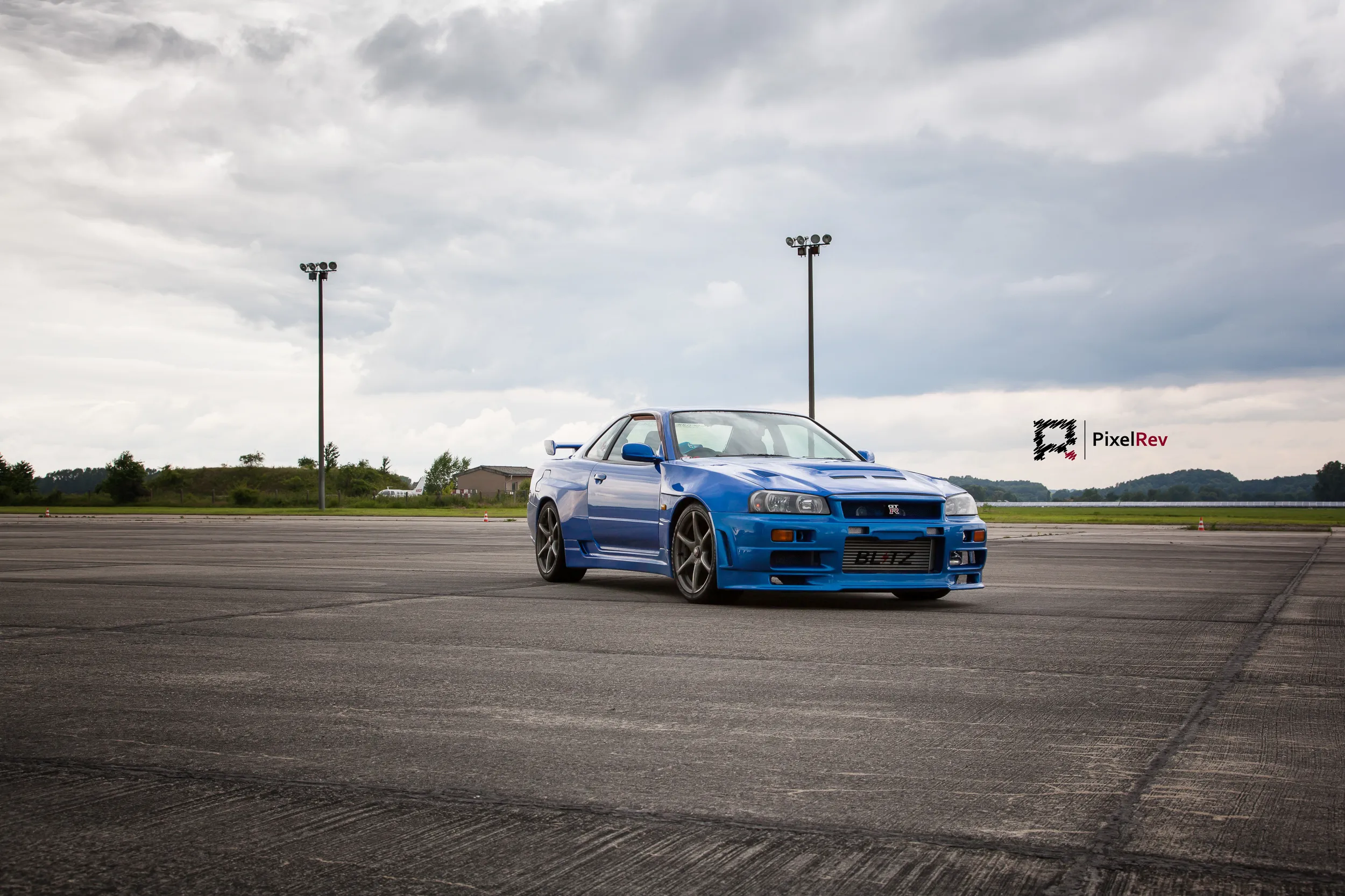Blauer Nissan Skyline R34 GT-R auf dem Rollfeld unter Wolkenhimmel