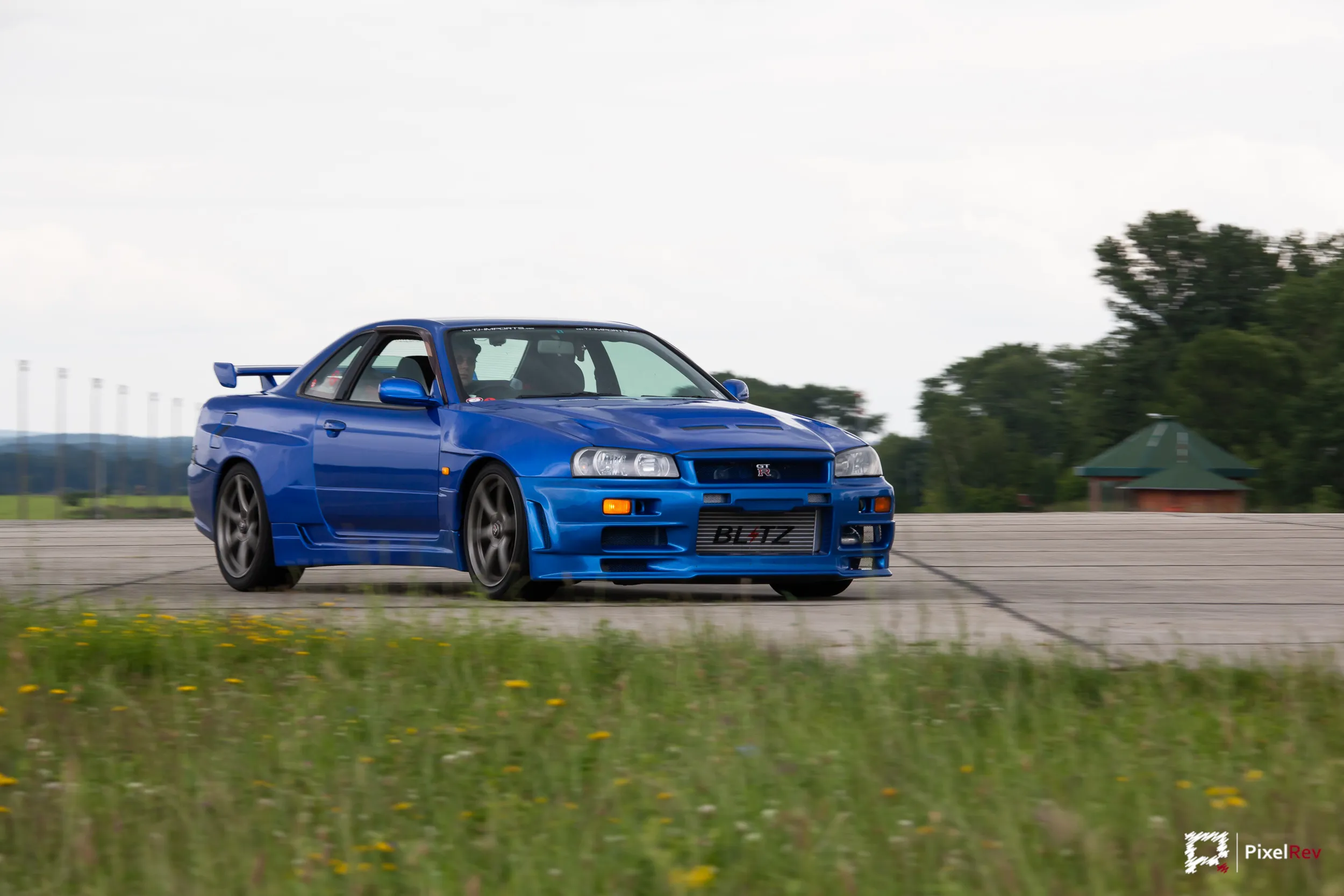 Blauer Nissan Skyline R34 GT-R auf dem Rollfeld, Gras im Vordergrund