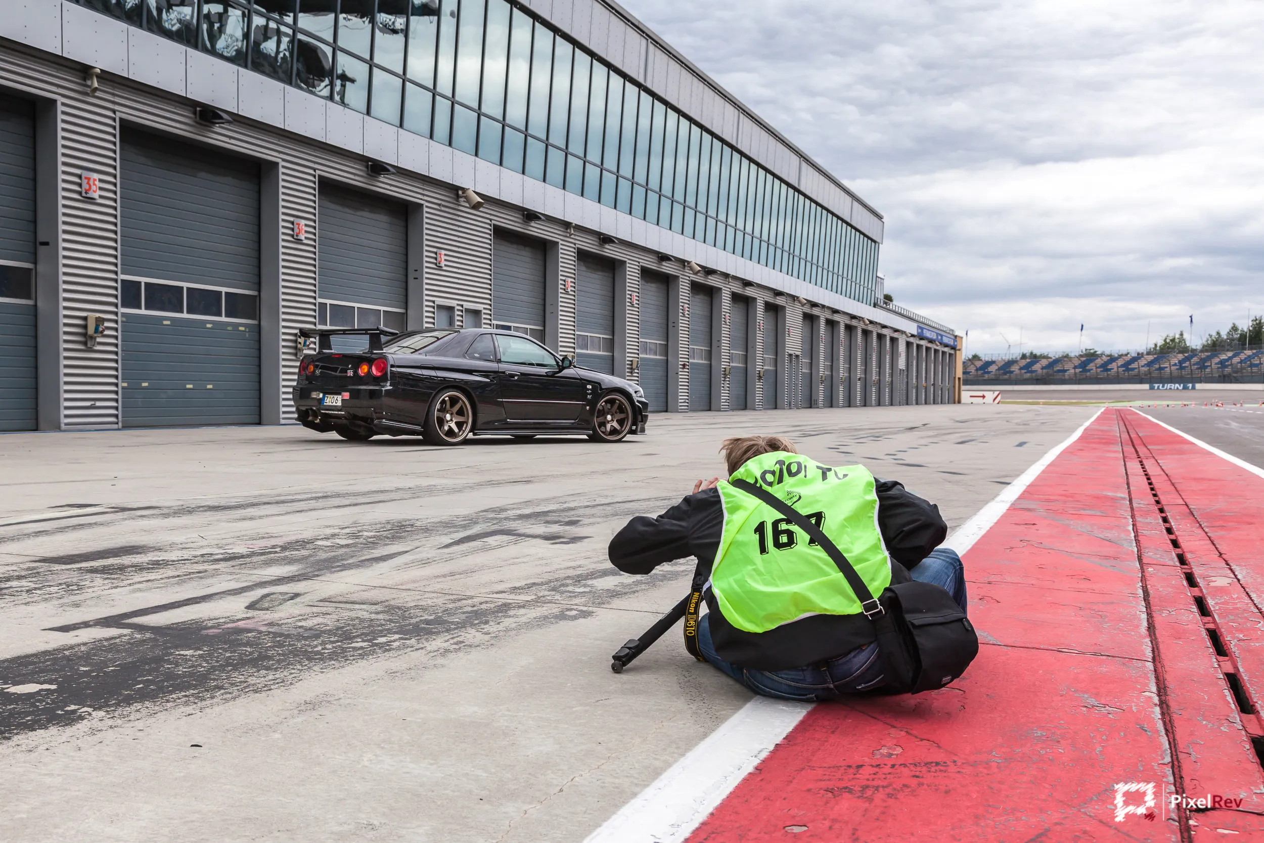 Fotograf kniet in der Boxengasse, dahinter der Nissan Skyline R34 GT-R Nismo Omori S1