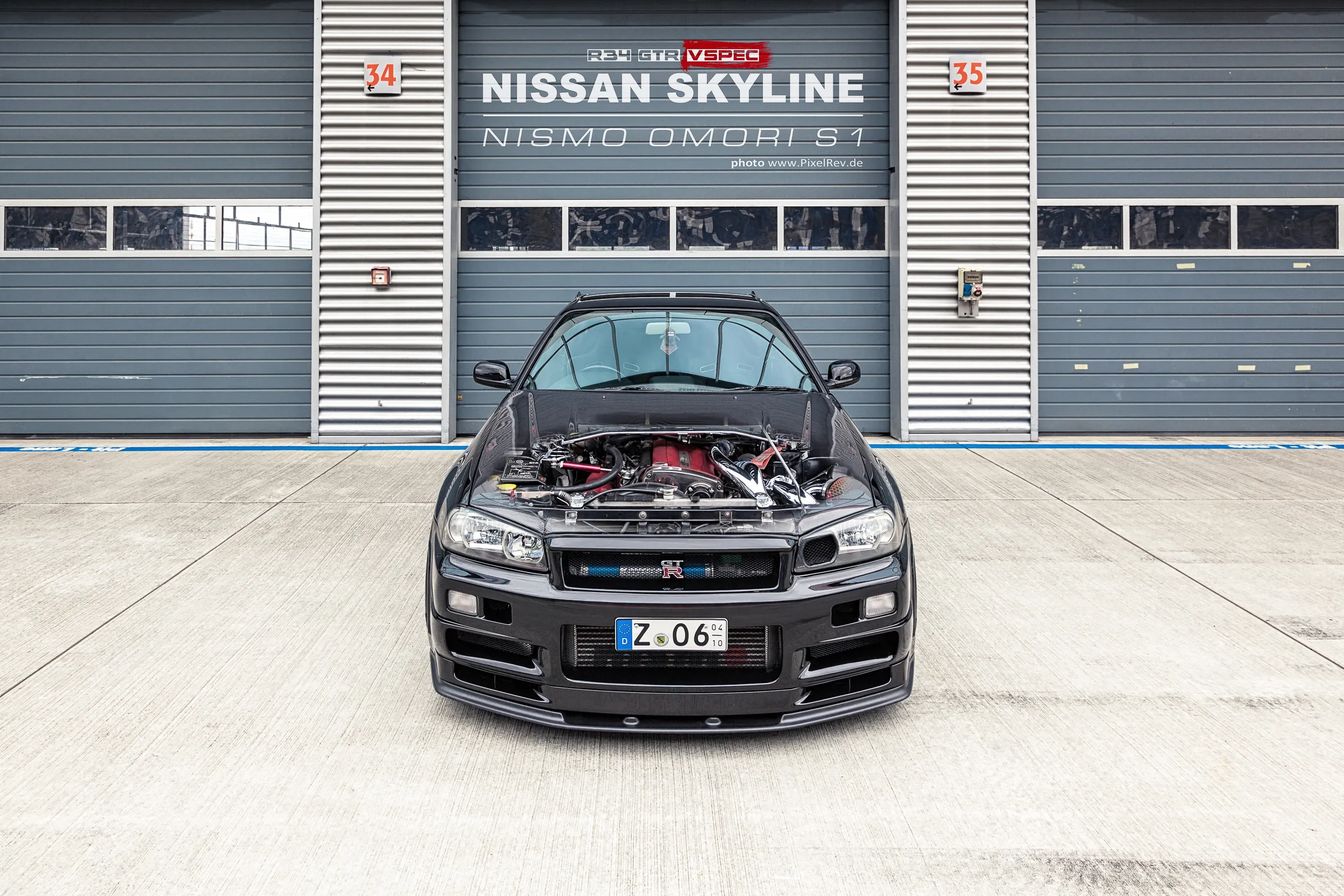 Nissan Skyline R34 GT-R Nismo Omori S1 mit geöffneter Motorhaube, Titel auf dem Rolltor