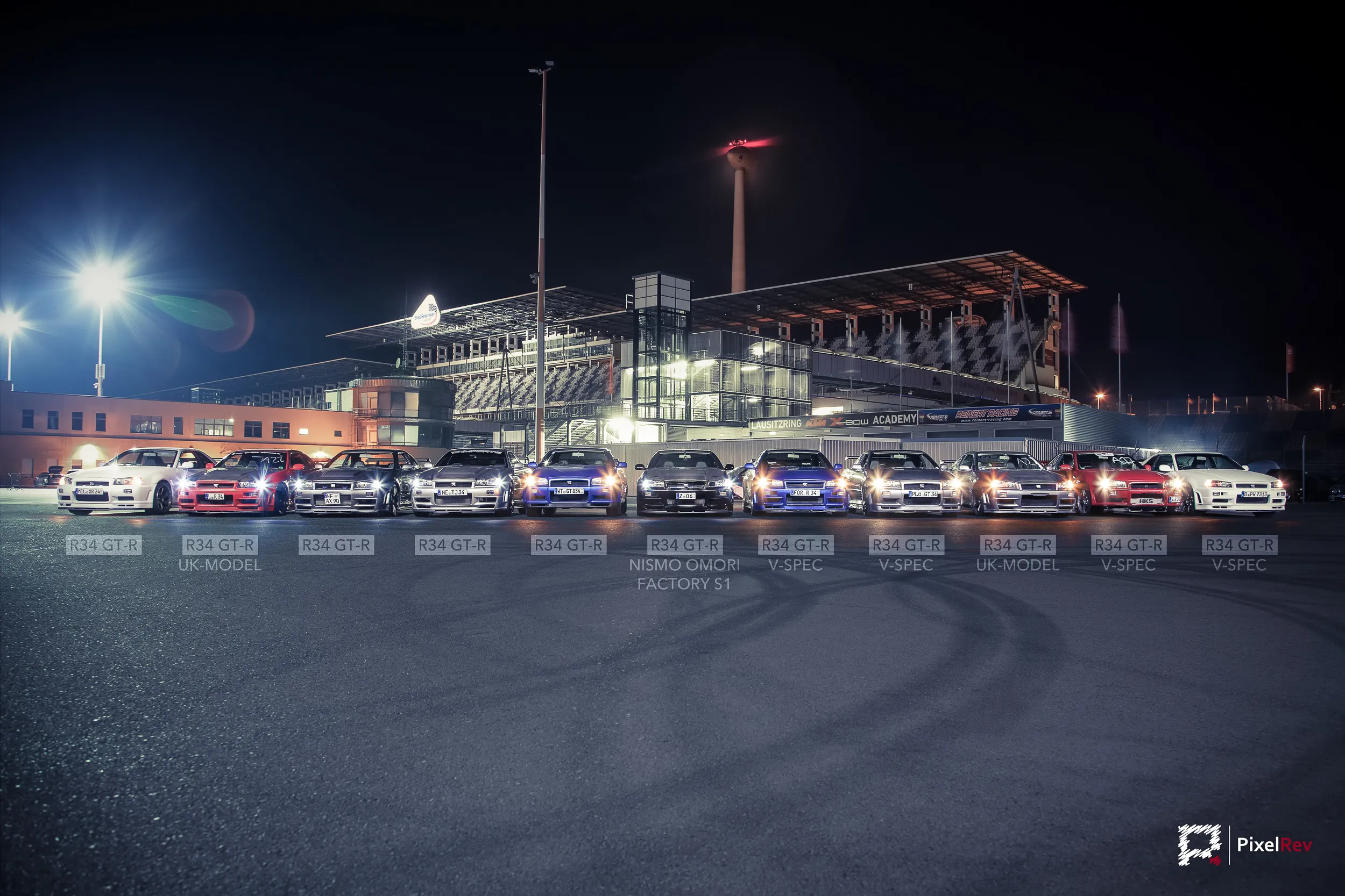 Nissan Skyline R34 GT-R in einer Reihe bei Nacht vor der Tribüne, mit Modellbezeichnungen