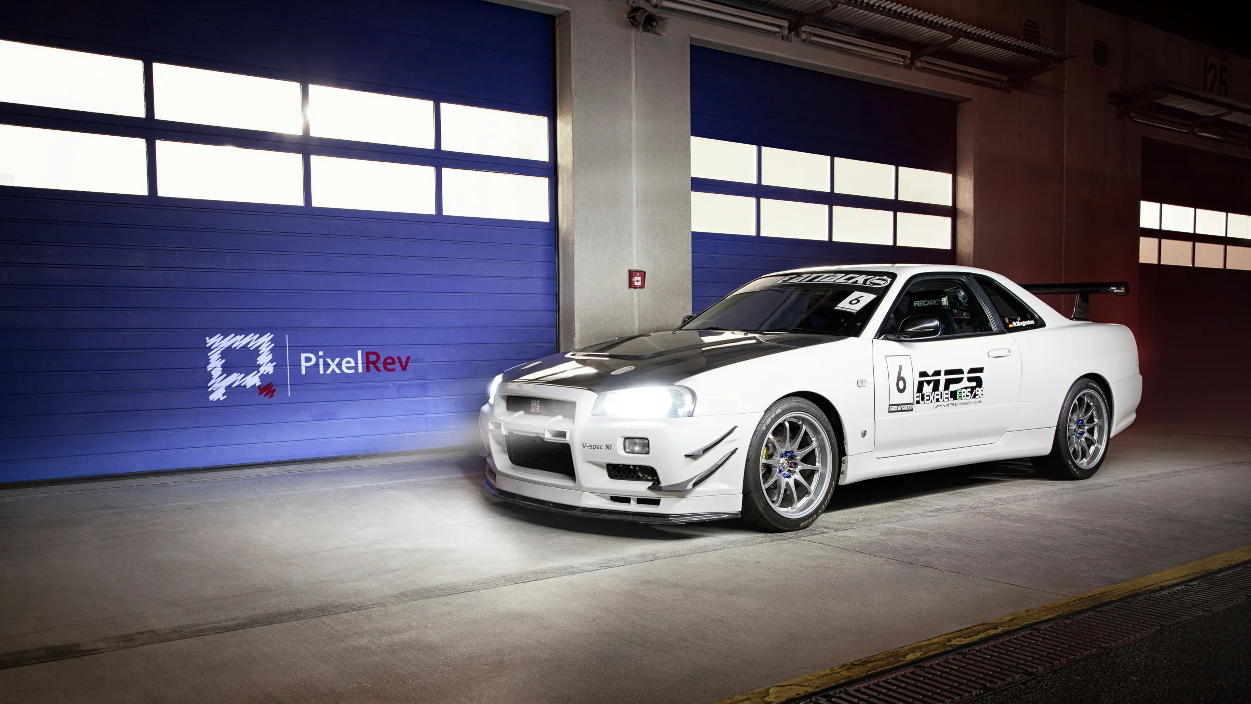 Weißer Nissan Skyline R34 GT-R mit Startnummer in einer Box bei Nacht