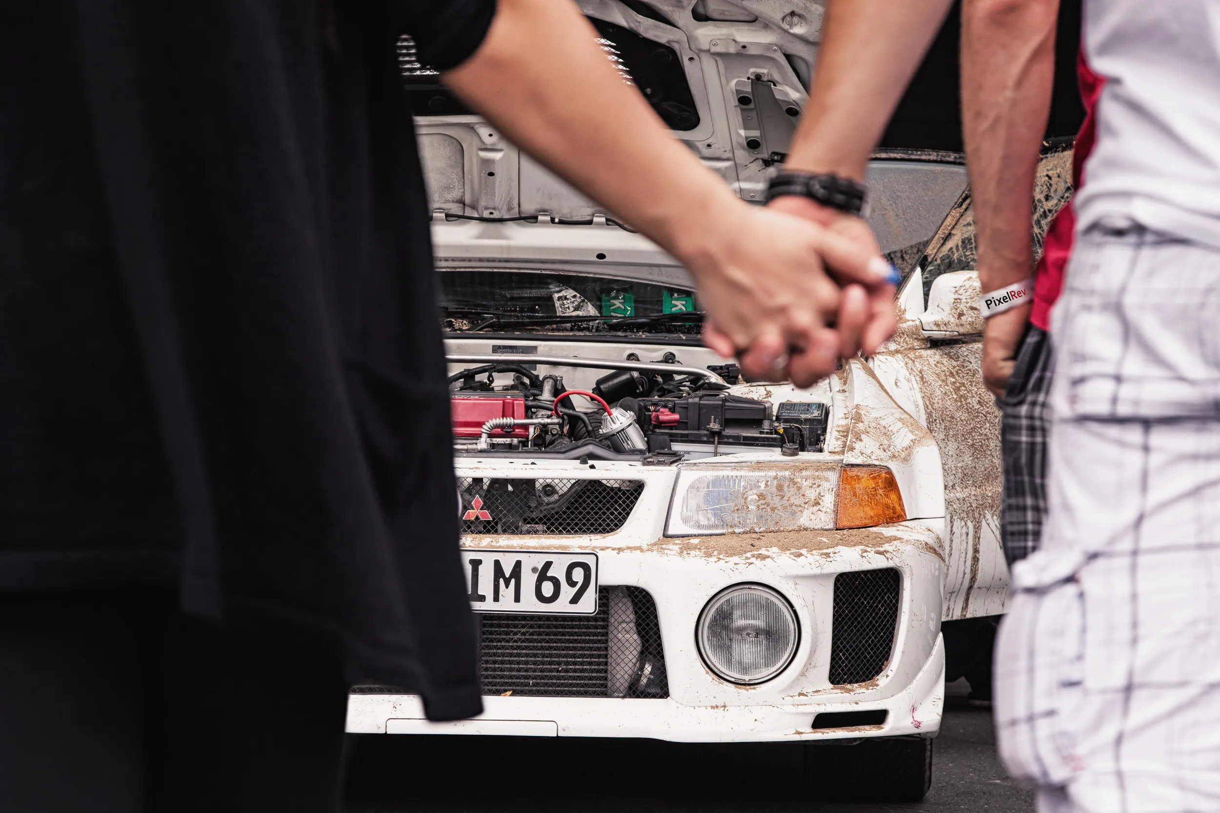Händchenhaltendes Paar vor einem verschmutzten Mitsubishi Lancer Evolution