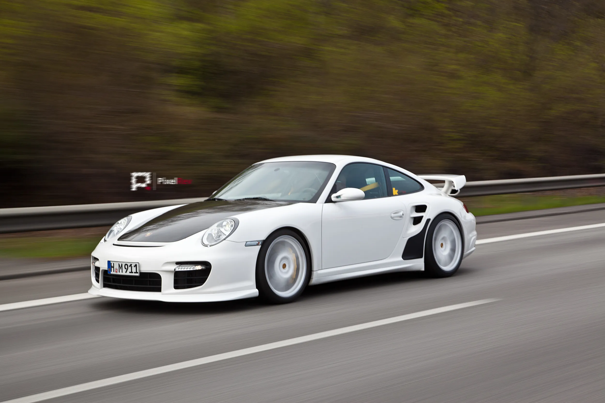 Weißer Porsche 911 GT2 mit Carbon-Motorhaube in Fahrt auf der Landstraße