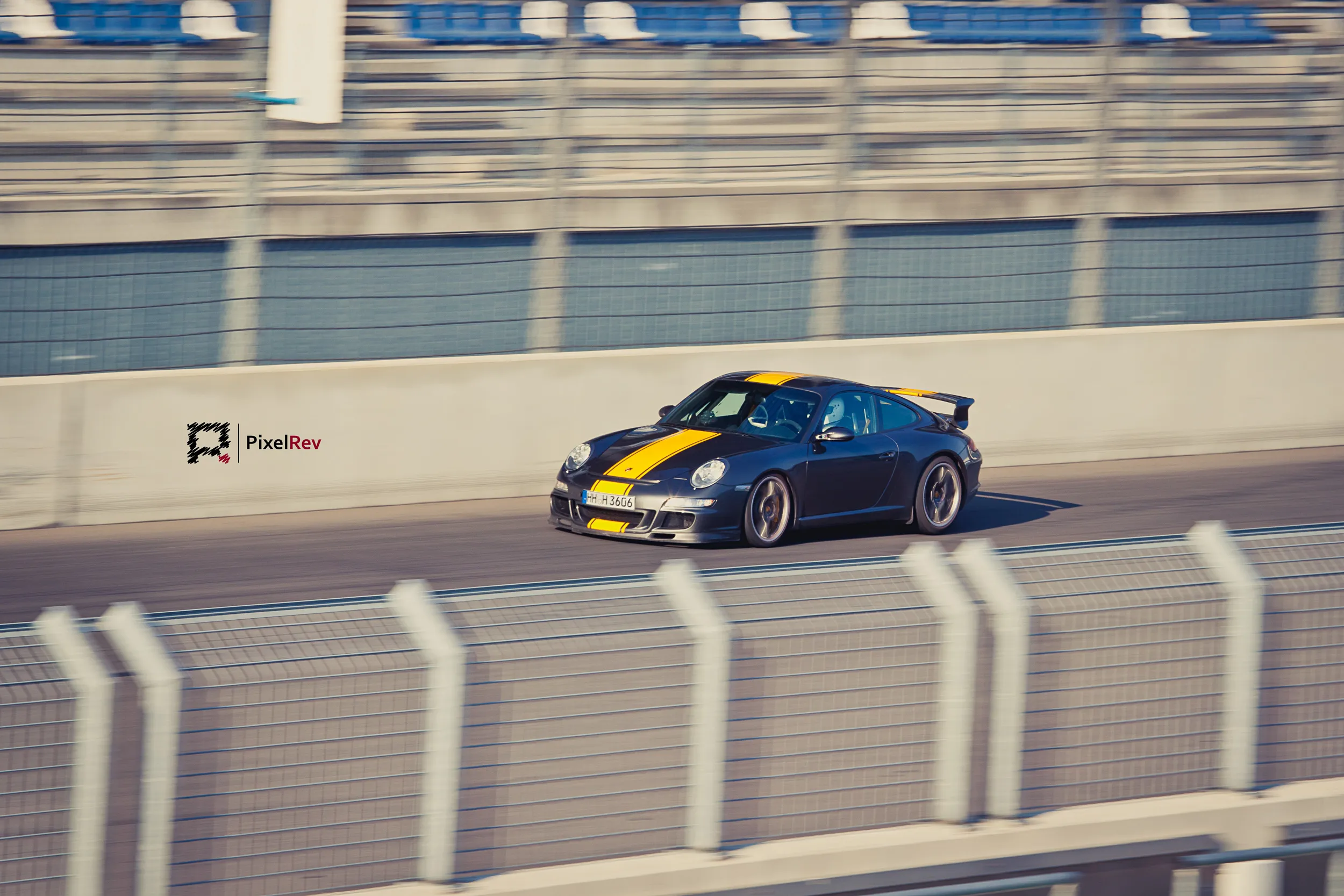 Dunkler Porsche 911 GT3 mit gelben Streifen im Mitzieher vor der Boxenmauer am Lausitzring