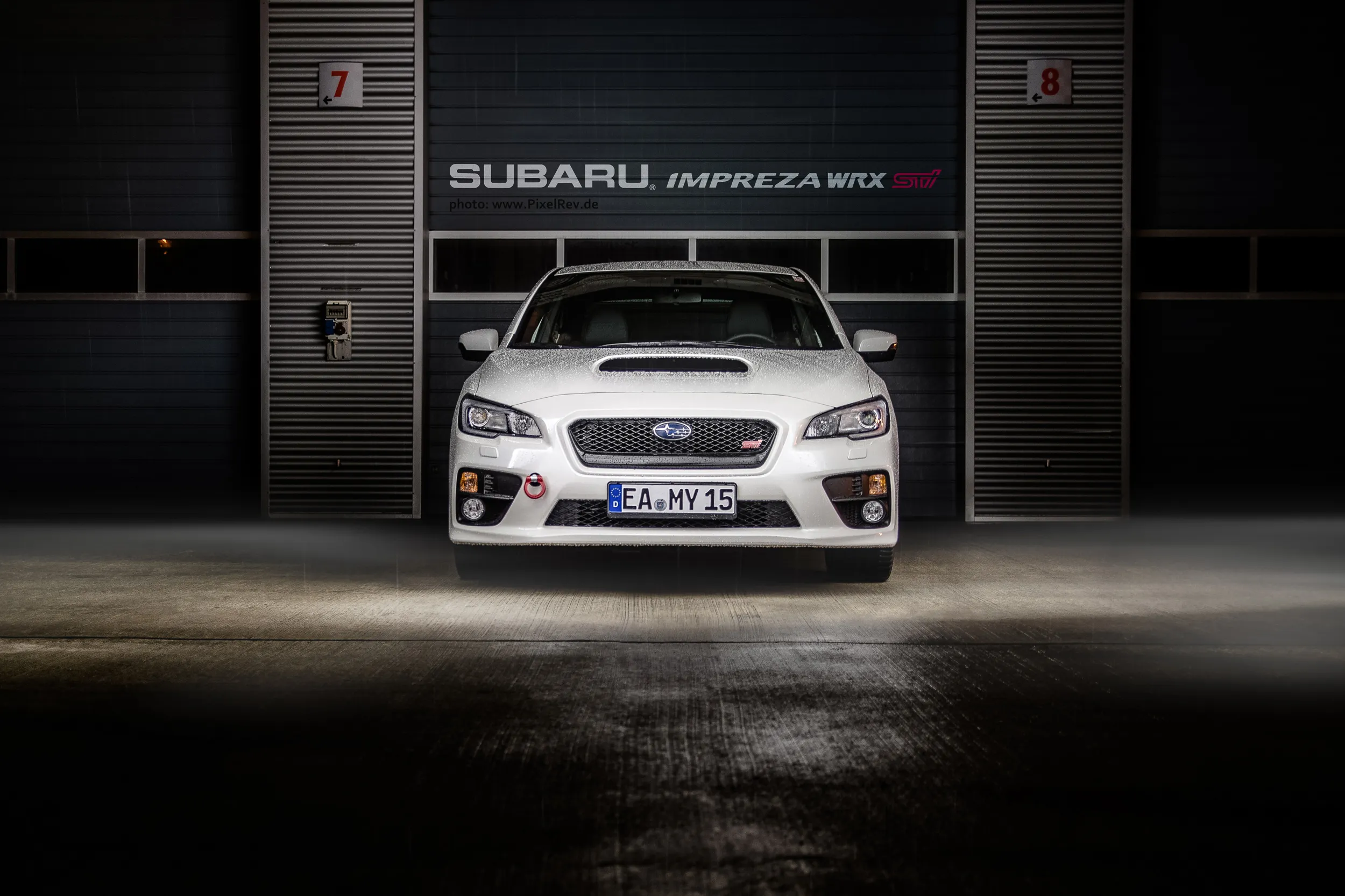 Weißer Subaru WRX STI frontal vor einer Box mit Impreza-WRX-Schriftzug