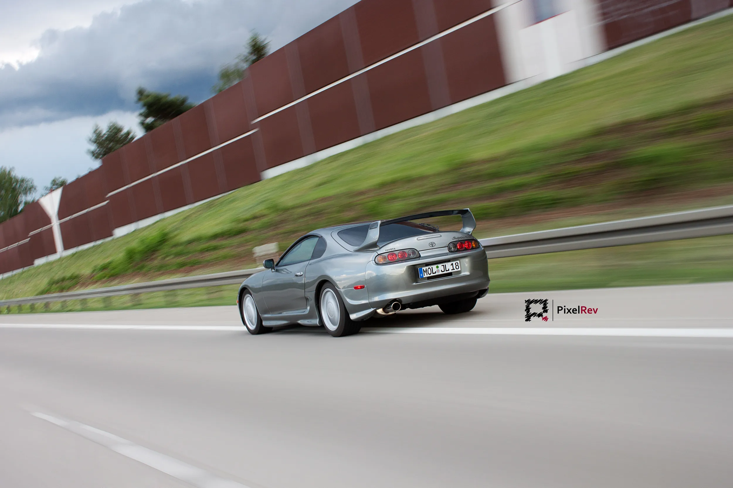 Silberner Toyota Supra Mk4 in Fahrt auf der Autobahn, Lärmschutzwand in Bewegungsunschärfe
