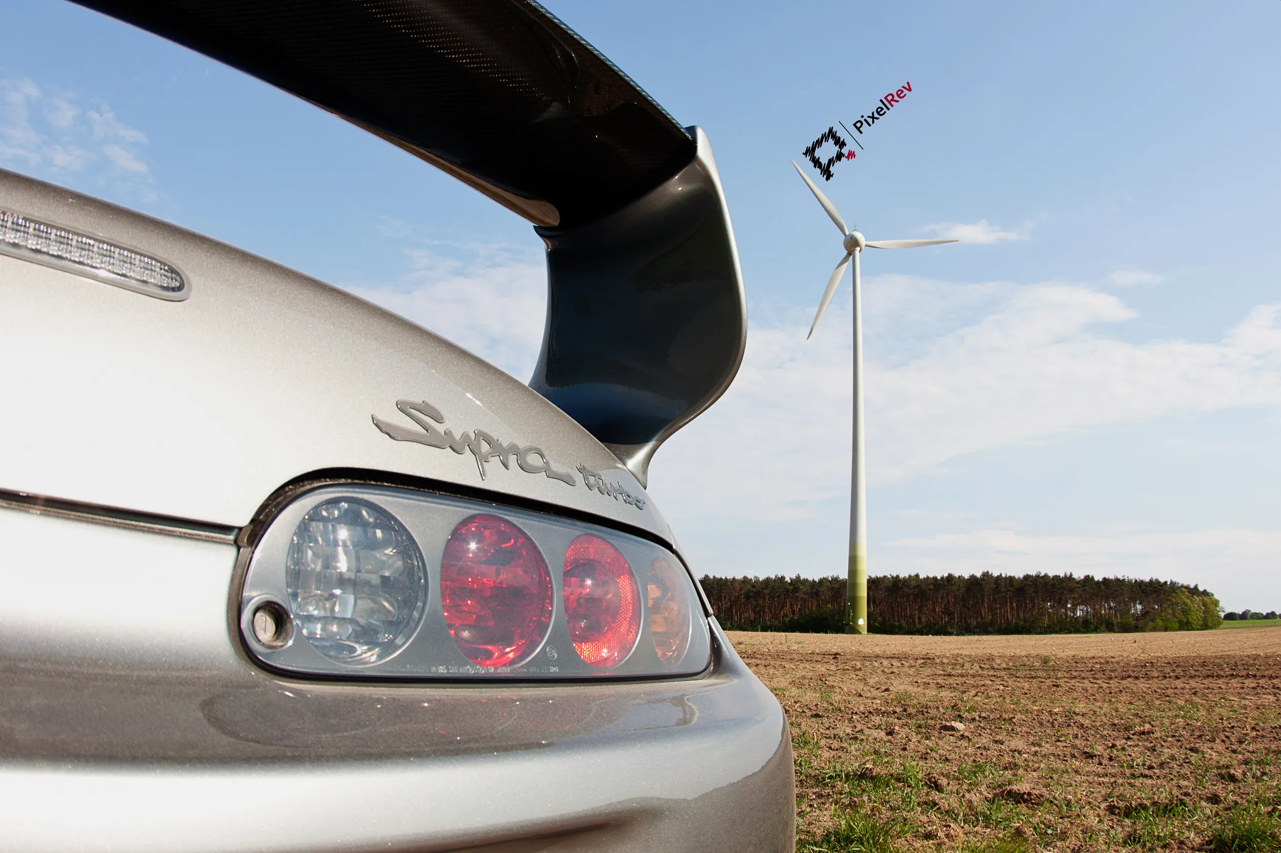 Rückleuchte und Supra-Schriftzug des silbernen Toyota Supra Mk4, dahinter ein Windrad
