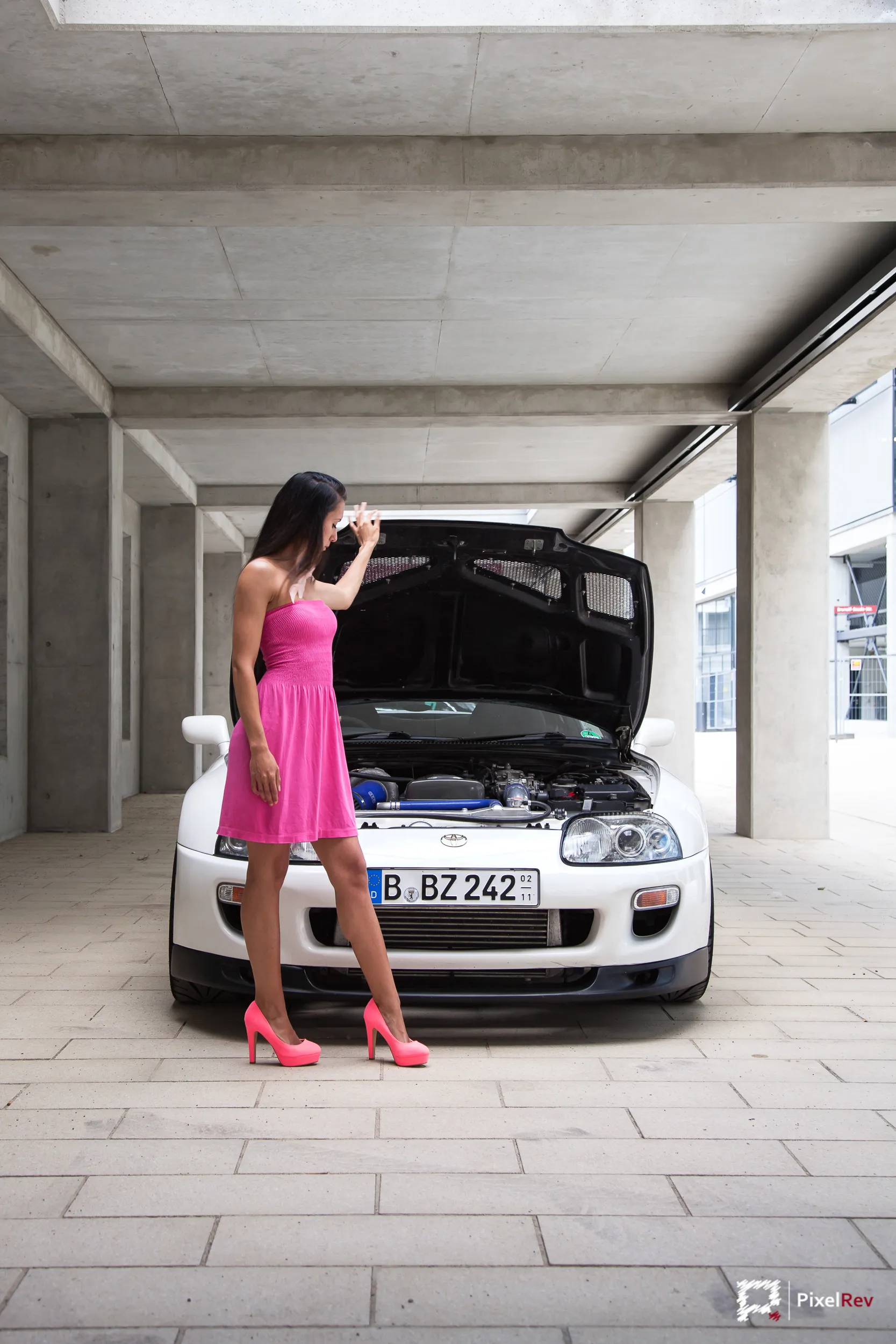Model in pinkem Kleid vor einem weißen Toyota Supra mit geöffneter Motorhaube
