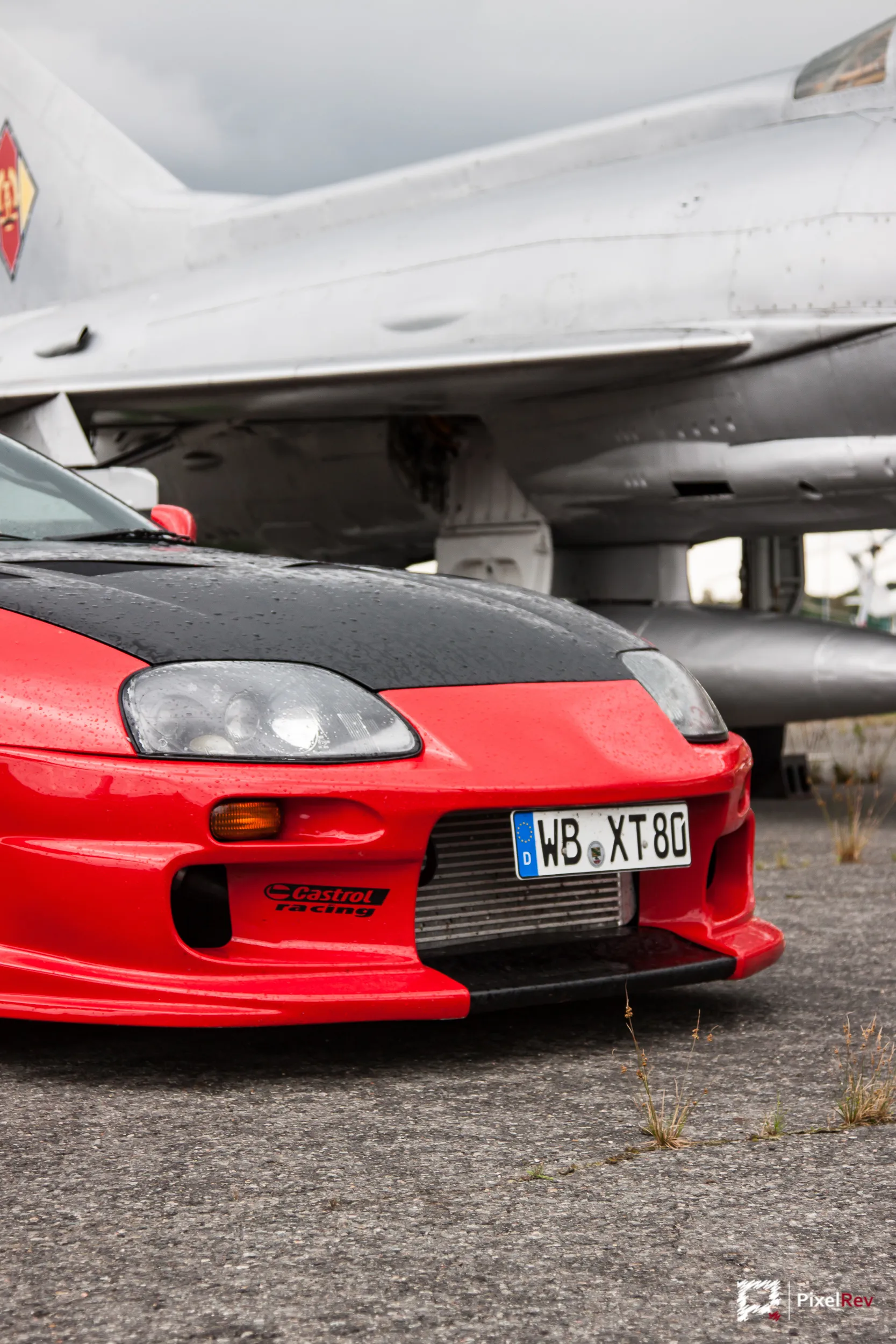 Front des roten Toyota Supra unter dem Flügel eines Kampfjets
