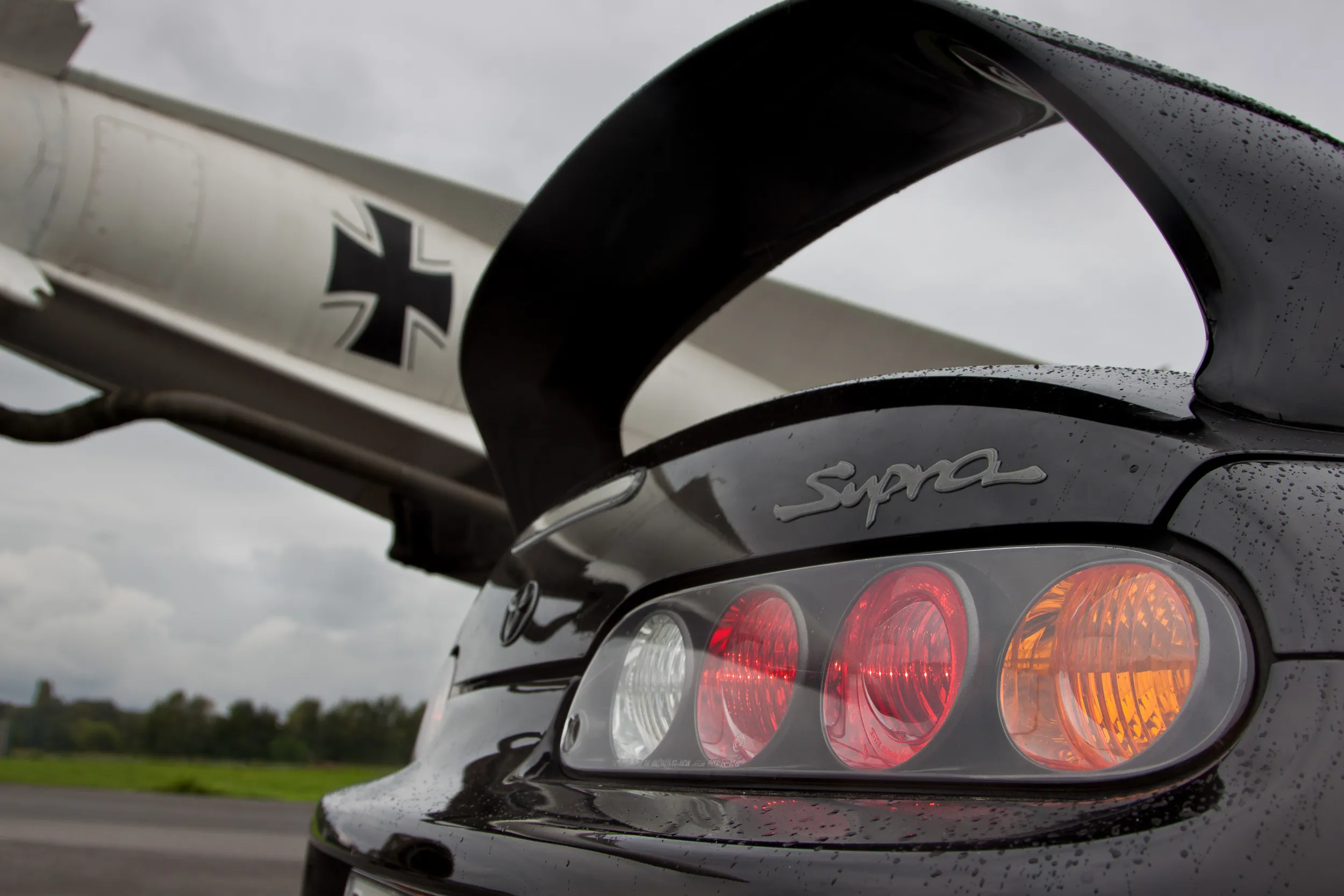 Rückleuchten und Supra-Schriftzug eines schwarzen Toyota Supra vor einem Flugzeugleitwerk